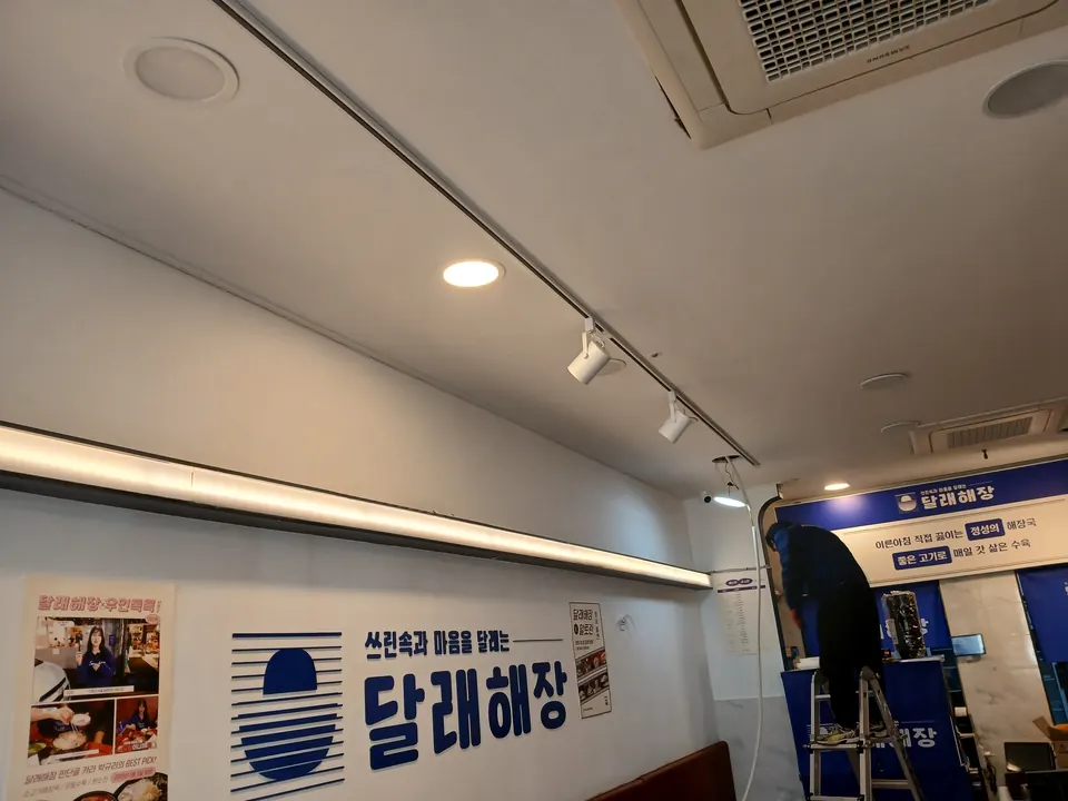 레일 조명과 벽면 라인 조명 설치 작업 중인 식당 벽