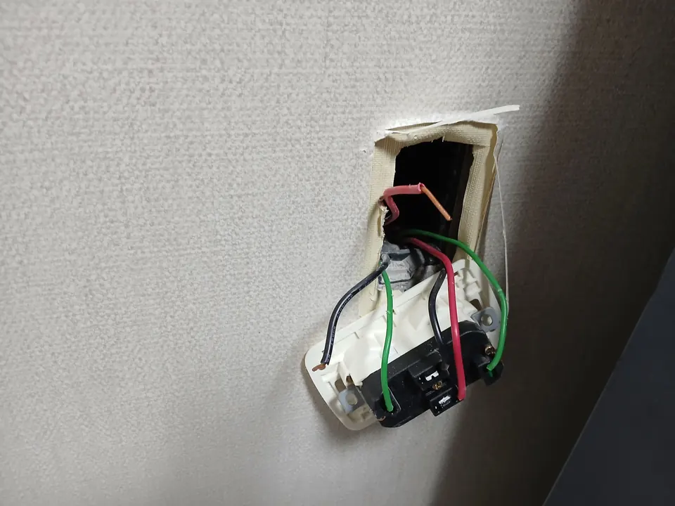 벽지 속에서 떼어낸 노후 콘센트와 드러난 내부 배선